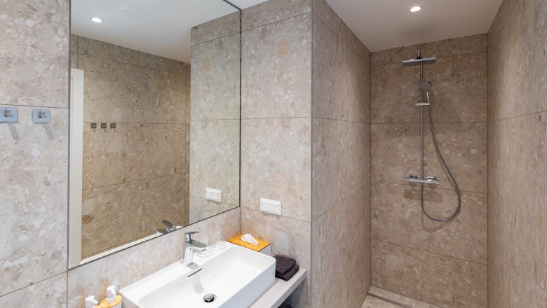 Modern bathroom with beige tiled wall, washbasin, mirror and rain shower.