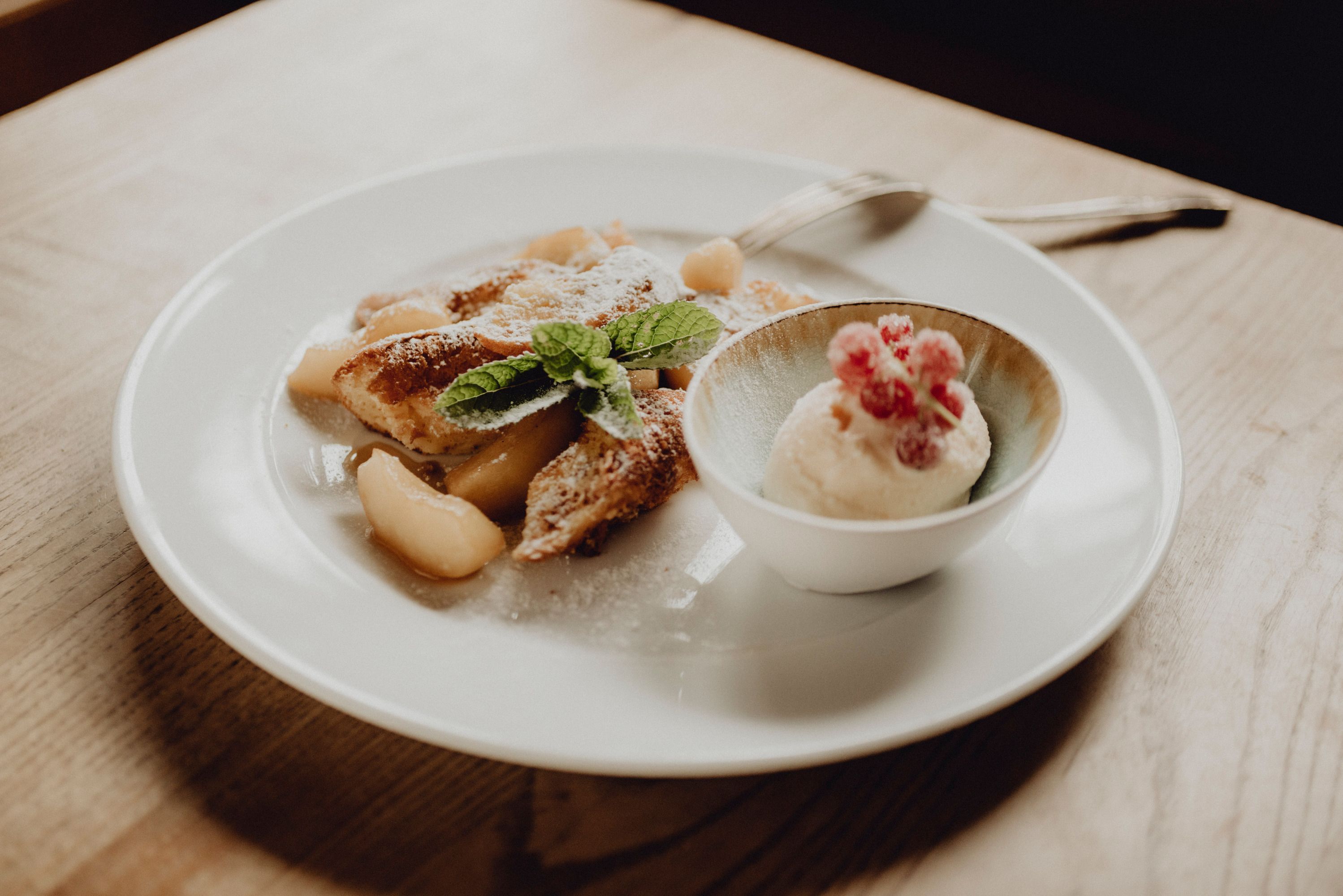 A plate of apple pancakes and a bowl of curd rum ice cream, garnished with mint leaves and red berries.