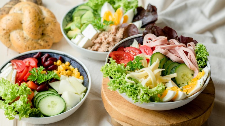 Three bowls of fresh salads, vegetables and eggs on a table.