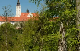 View of a monastery building with tower behind trees in Altenburg Abbey Forest.