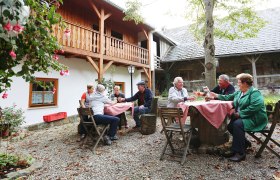 People sit at wooden tables outside in front of a traditional building.
