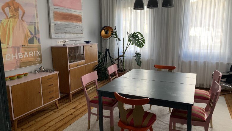 Dining area with table, chairs, chests of drawers and works of art on the wall.