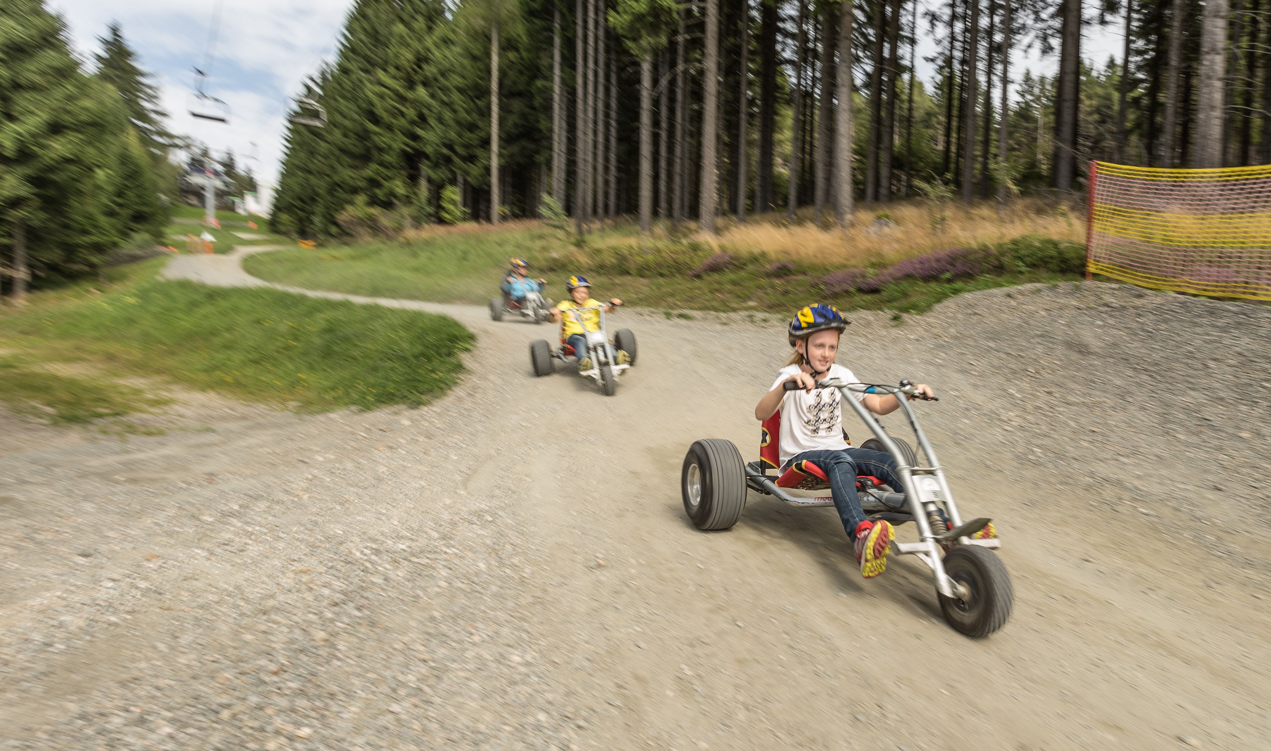 Children are riding mountain carts along a path.