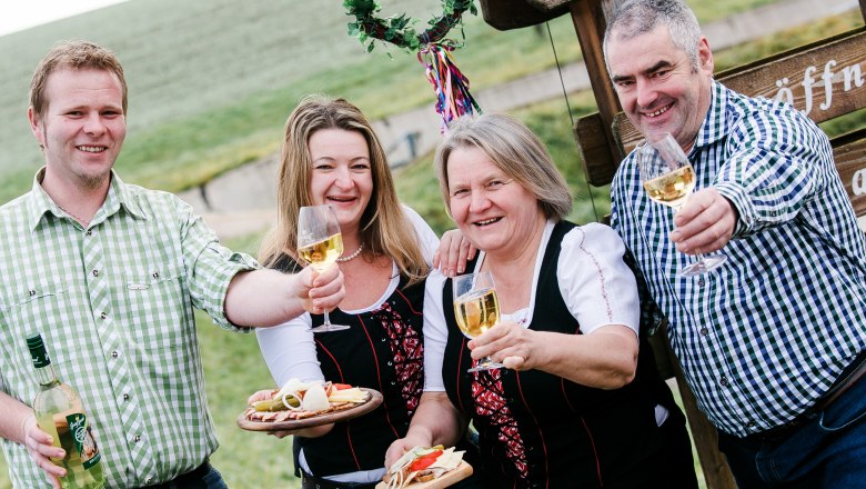 Four people clink glasses of wine outside in front of a sign.