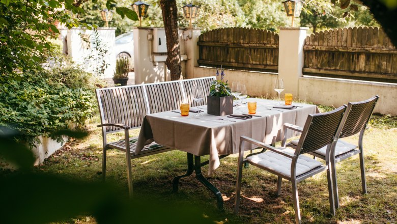 Set table in the garden with chairs and benches under trees.