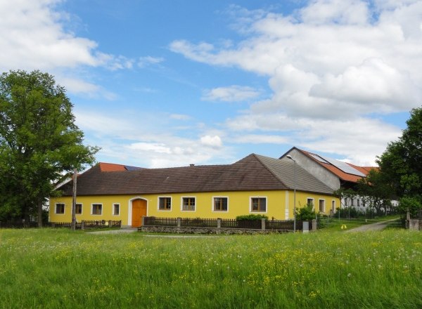 Weißensteiner organic farm, © Wolfgang Weißensteiner Yellow farmhouse on a green meadow with blue sky and clouds.