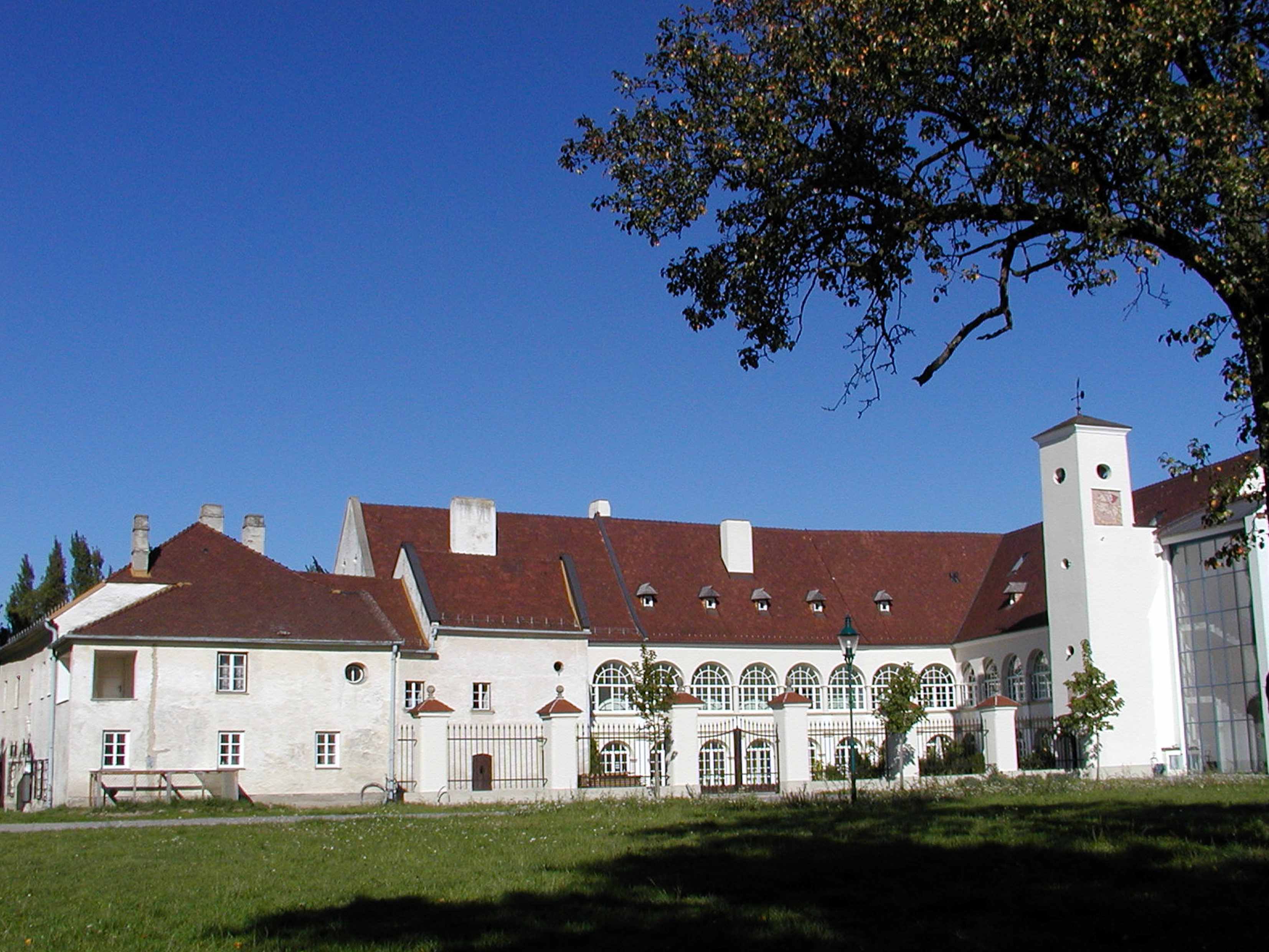Katzelsdorf Castle with its red roof and white walls, surrounded by trees and lawns.