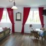 A traditionally furnished room with a wooden floor, red curtains and a table with two dolls in traditional costume.