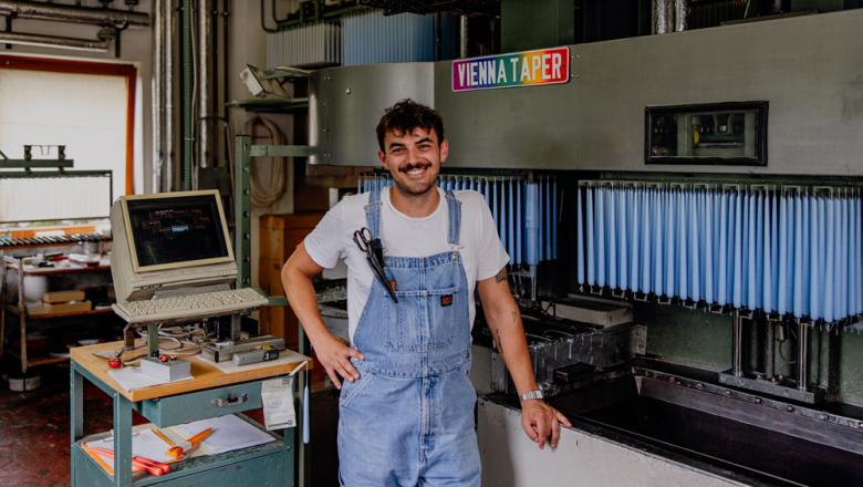 A man in dungarees stands smiling in front of a candle-dunk installation with blue candles.