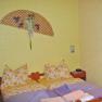 A cozy bedroom with yellow walls, a double bed with patterned pillows and a decorative wall fan.