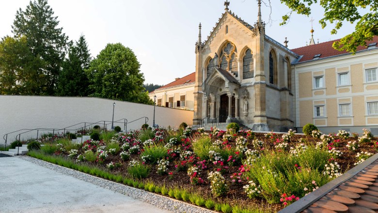 A church with Gothic elements and a well-tended garden full of flowers in the foreground.