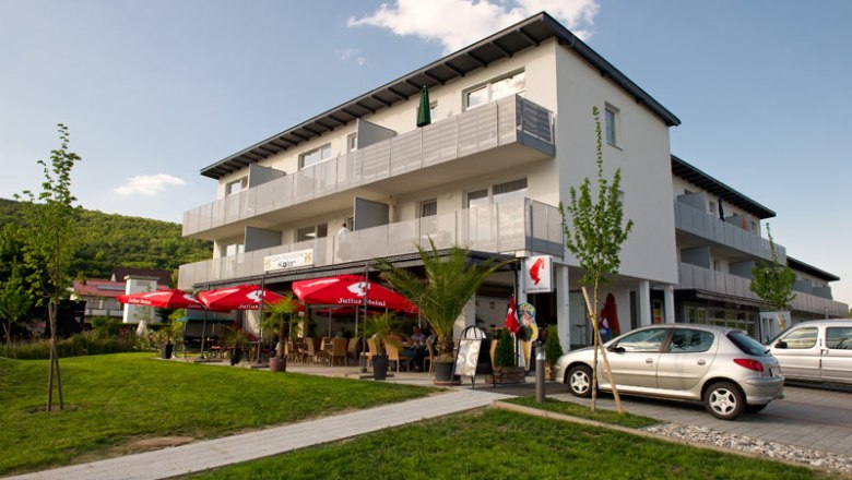 Exterior view of a modern building with a caf&eacute; and red parasols.