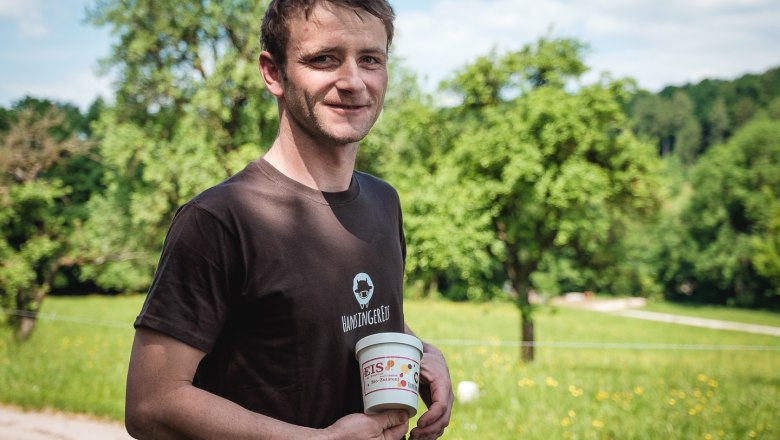 A man holds a cup of organic ice cream in a green landscape.
