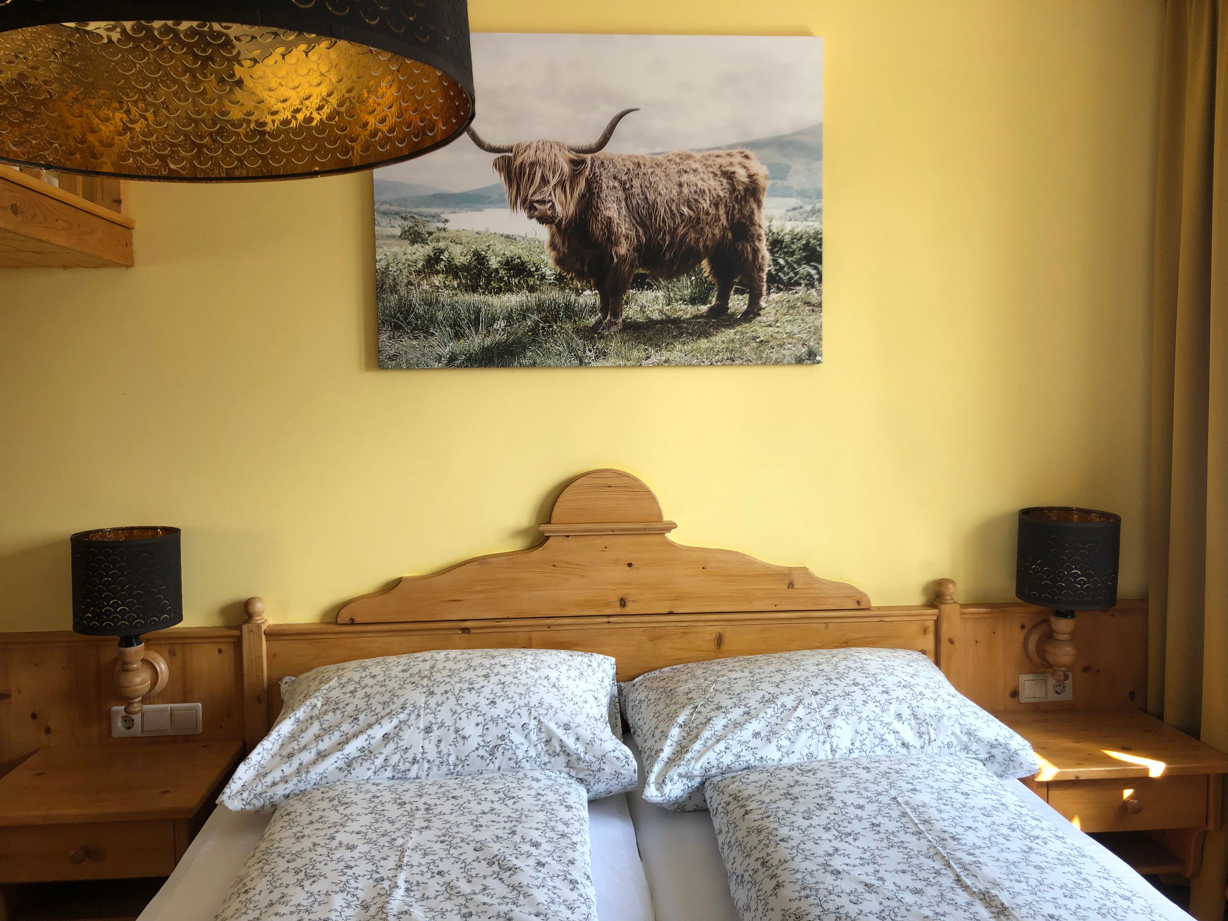 Cozy bedroom with wooden furniture, double bed and picture of a highland cattle on the wall.