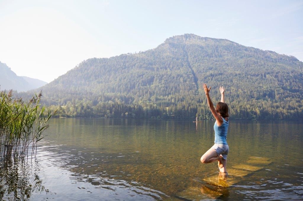 A woman doing yoga in a lake with a mountain in the background.