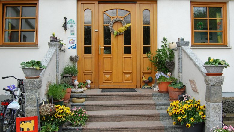 Front of a house with wooden door, staircase and floral decoration.