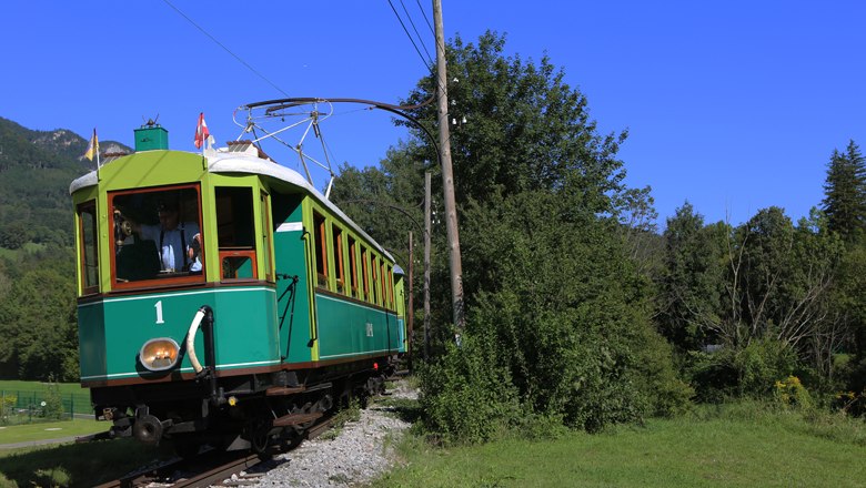 Historic green train travels through a green landscape under a blue sky.