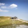 A mountain hut on a hill with a blue sky and clouds in the background.
