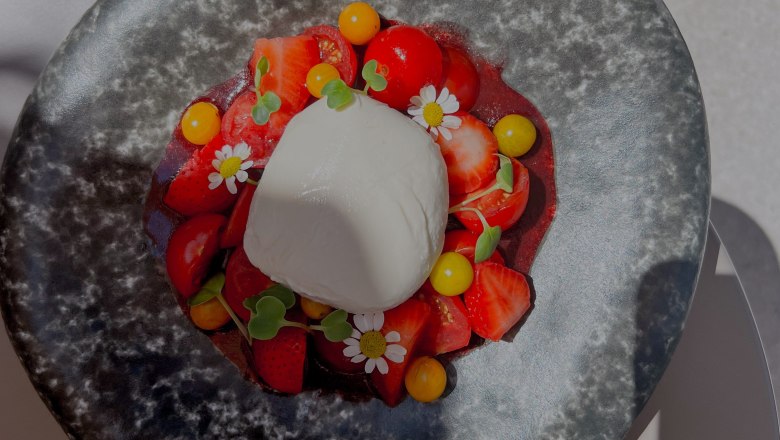 A plate of burrata, strawberries, tomatoes and edible flowers.