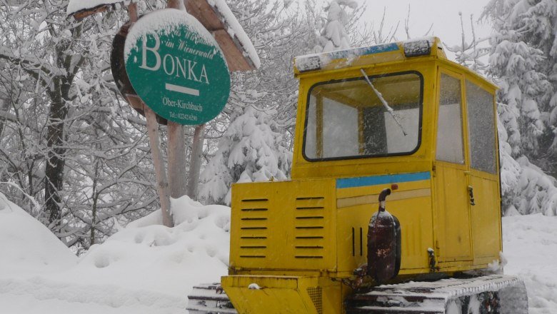 Yellow snow vehicle in the snow in front of a sign with the inscription 'Bonka' in Oberkirchbach.