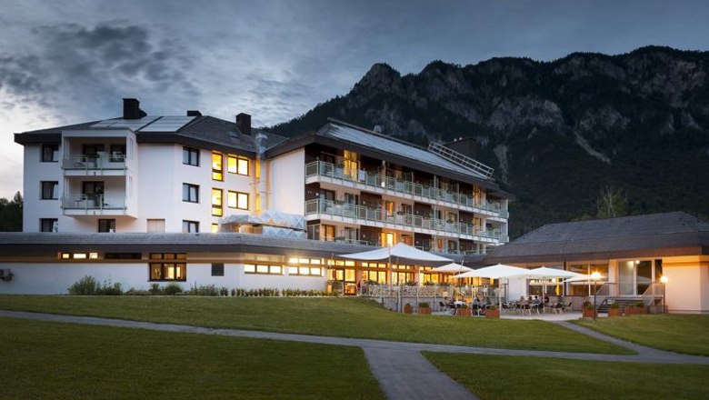 A hotel building in a mountainous landscape at dusk, illuminated with warm light.
