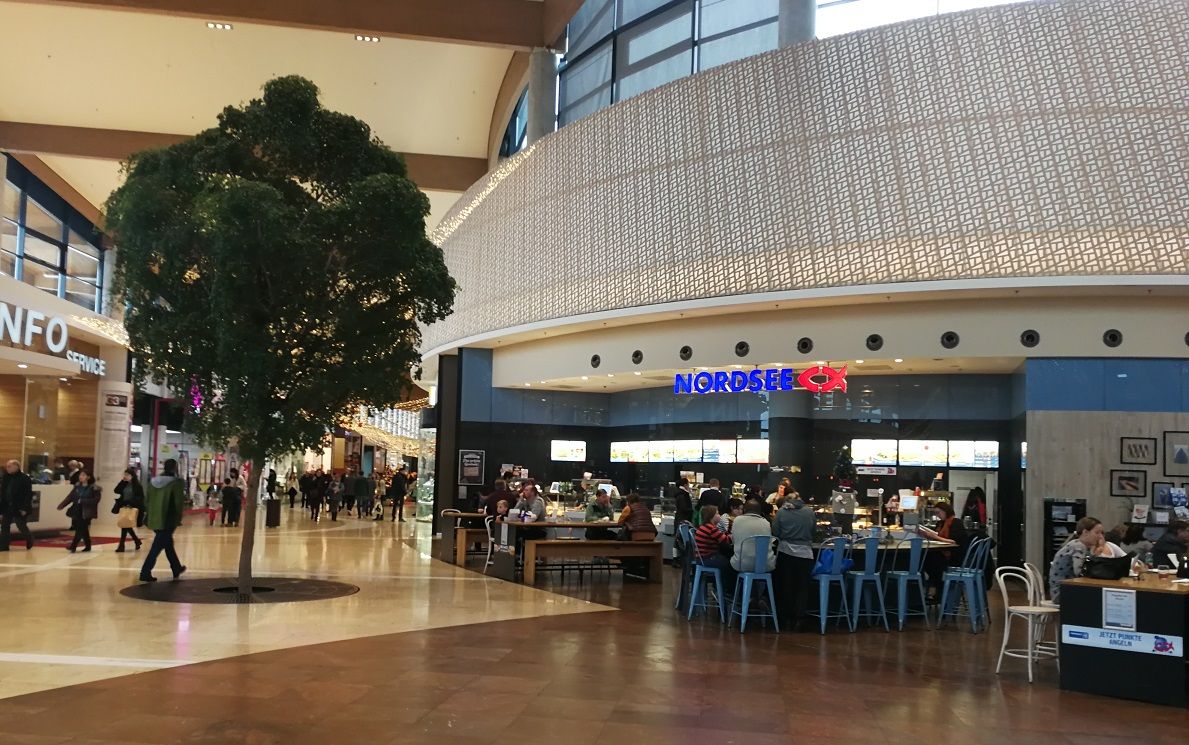 Interior view of a shopping center with a North Sea restaurant and a tree in the middle.