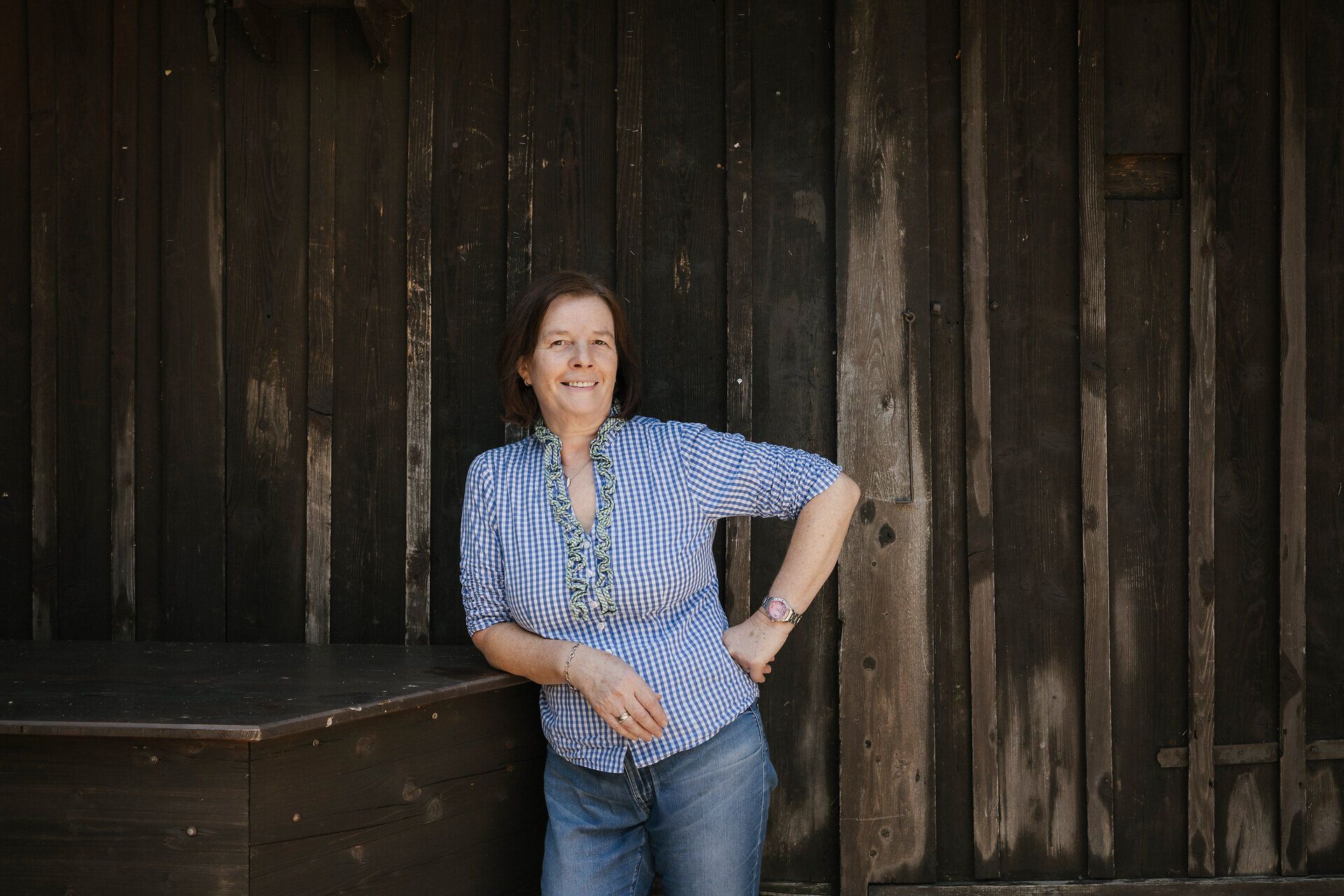 A smiling employee is leaning against a wooden wall at the Hengsthütte on Schneeberg