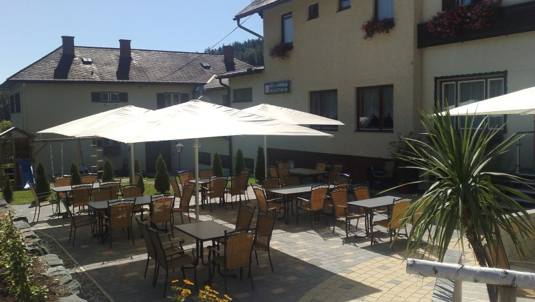 Outdoor area of a guesthouse with tables, chairs and parasols.