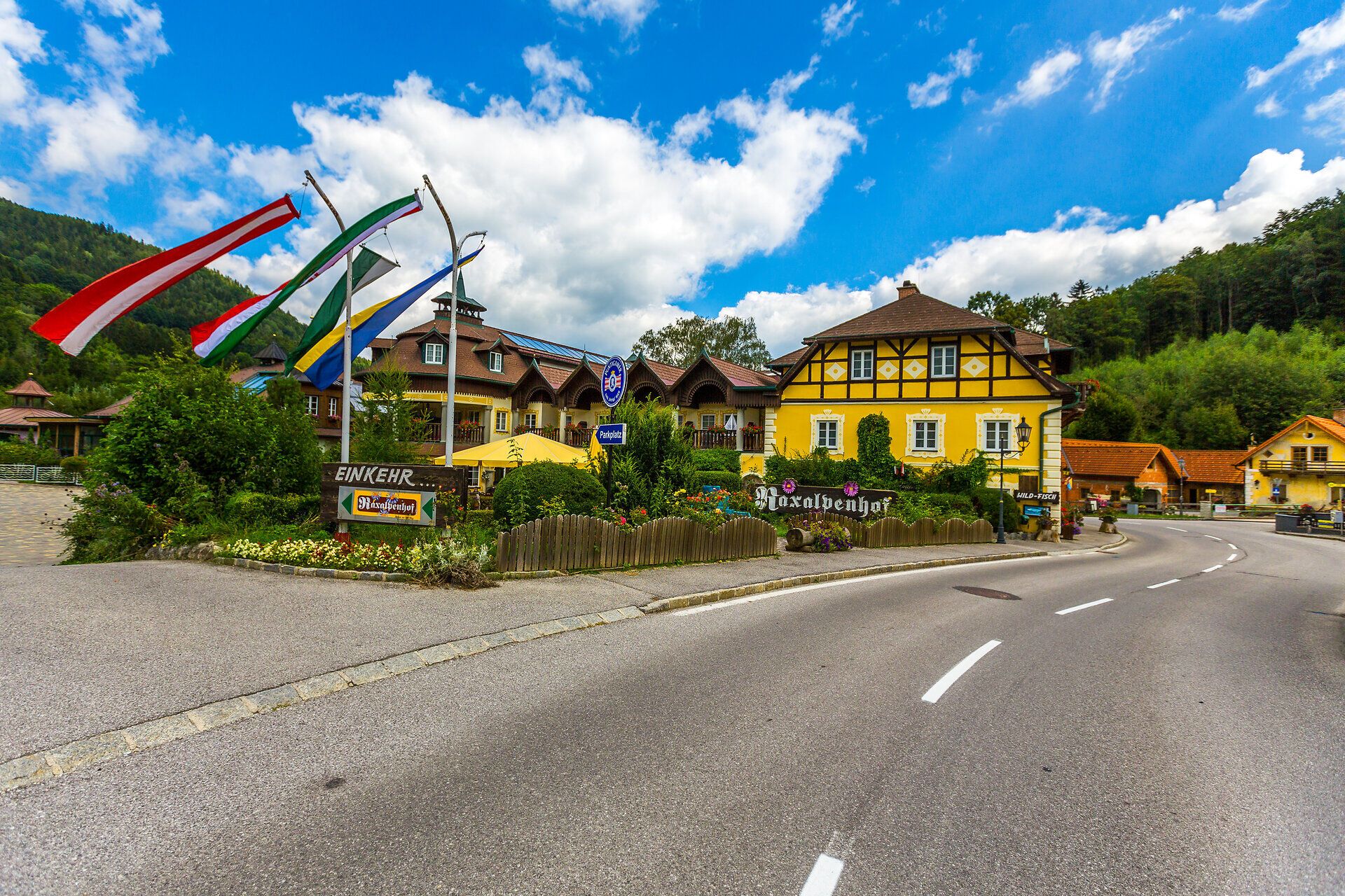 Raxalpenhof is located directly on the local road, there is a blue fountain in front of the house, flowers and shrubs line the balconies and the entire front area of the house