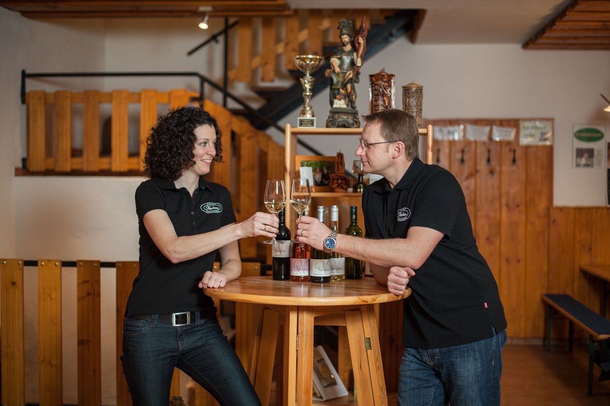 Two people clink glasses of wine at a wooden table.