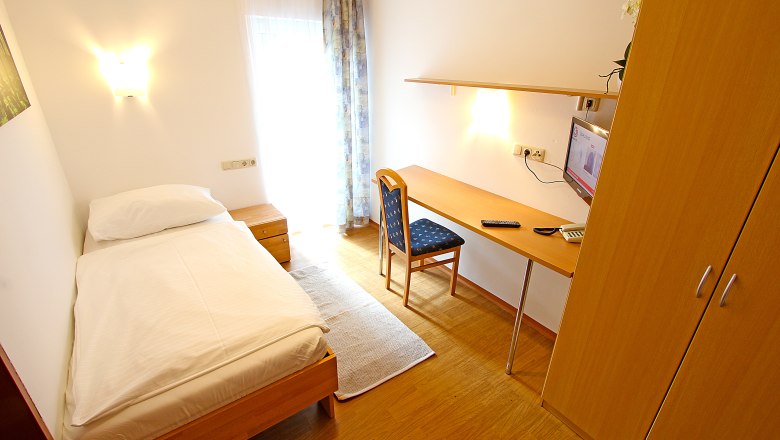 A simply furnished single room with bed, desk, chair and TV.