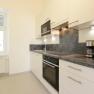 Modern kitchen with white cupboards, gray worktop, oven, microwave and coffee machines.