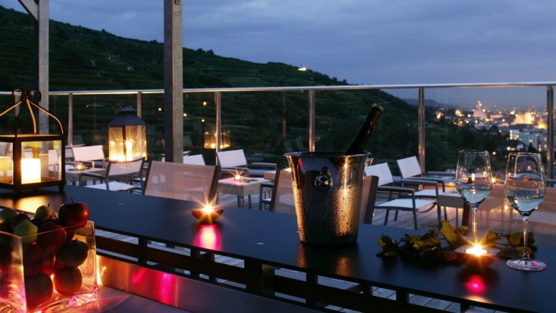 Evening terrace with candlelight, glasses of wine and a view of a city.