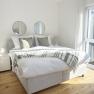 Bright bedroom with double bed, two round mirrors on the wall and large windows.