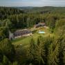 Aerial view of a forester's lodge in the middle of a dense forest with adjoining pool and meadow.