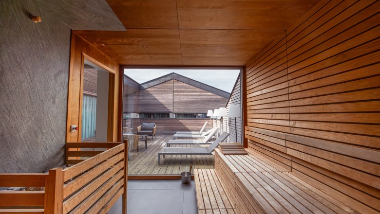 Interior view of a sauna overlooking a terrace with sun loungers and wooden walls.
