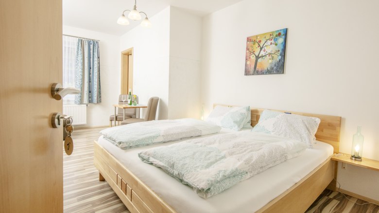 A bright guest room with a double bed, table, chairs and a colorful mural.