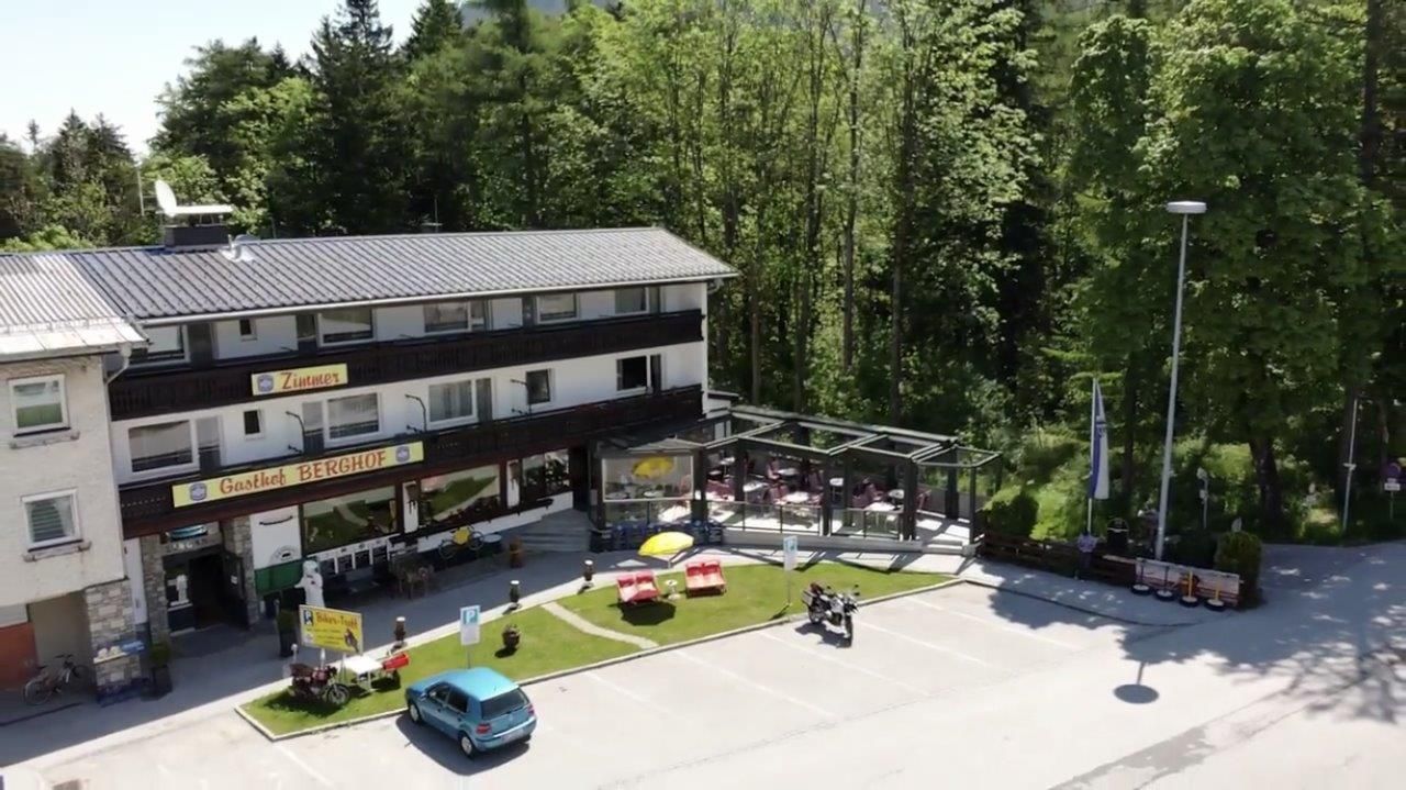 Exterior view of Gasthof Berghof with terrace and parking lot, surrounded by trees.