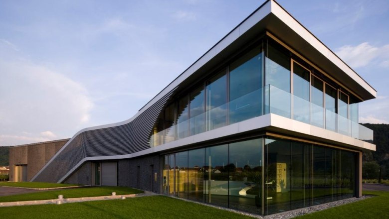 Modern building with glass façade and curved roof, surrounded by green meadows.