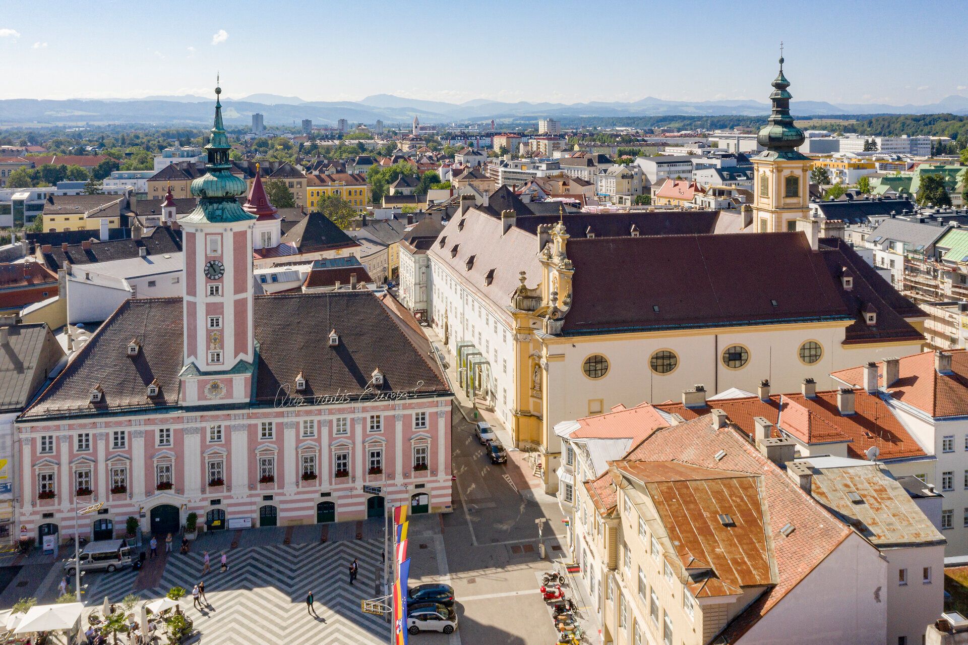 Der Rathausplatz in St. Pölten strahlt eine einladende Atmosphäre aus, umgeben von historischen Gebäuden und lebhaften Straßen. Die sanften Hügel im Hintergrund bieten einen malerischen Kontrast zur urbanen Szenerie und laden dazu ein, die Schönheit der Stadt zu erkunden.