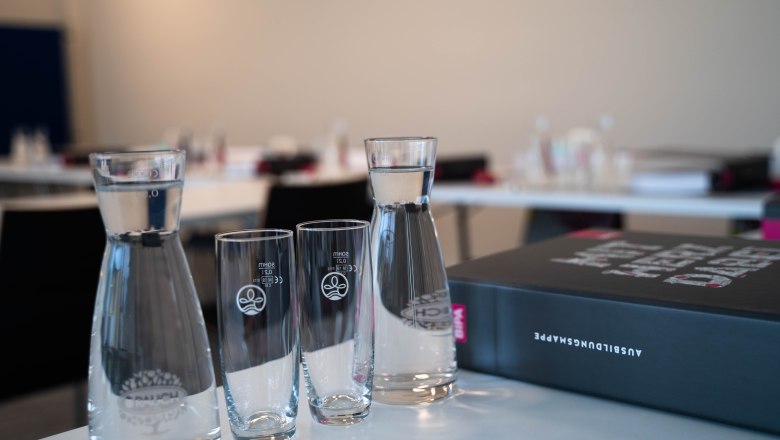 A seminar room with water carafes, glasses and a folder on a table.