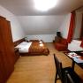 A simply furnished room with a double bed, sofa, table and chair. Wooden furniture and orange curtains dominate the room.