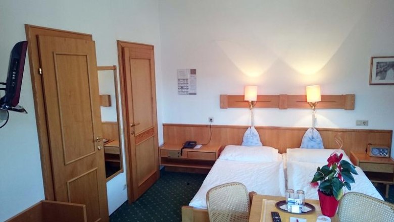 A hotel room with two single beds, wooden furniture and green carpeting.