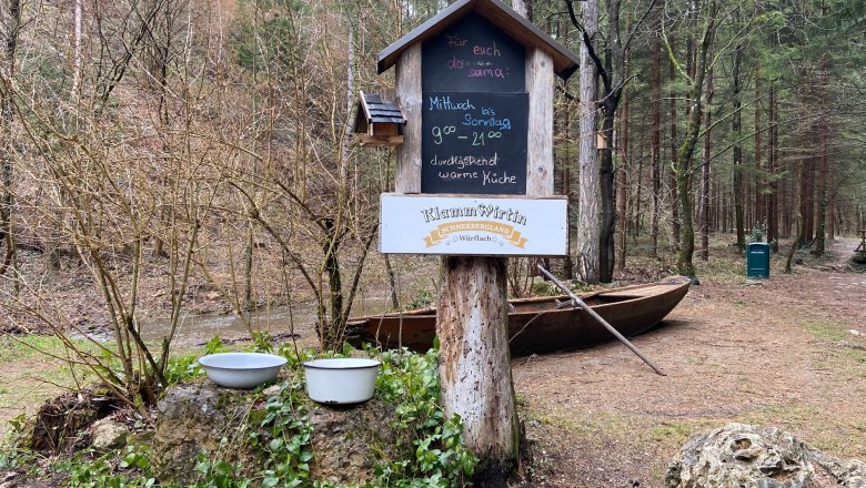 Signpost in the forest with the opening hours of the gorge landlady, surrounded by trees and a boat.