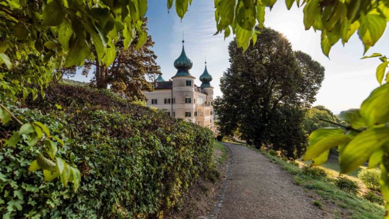 Artstetten Castle with green onion domes, surrounded by trees and a path in the foreground.