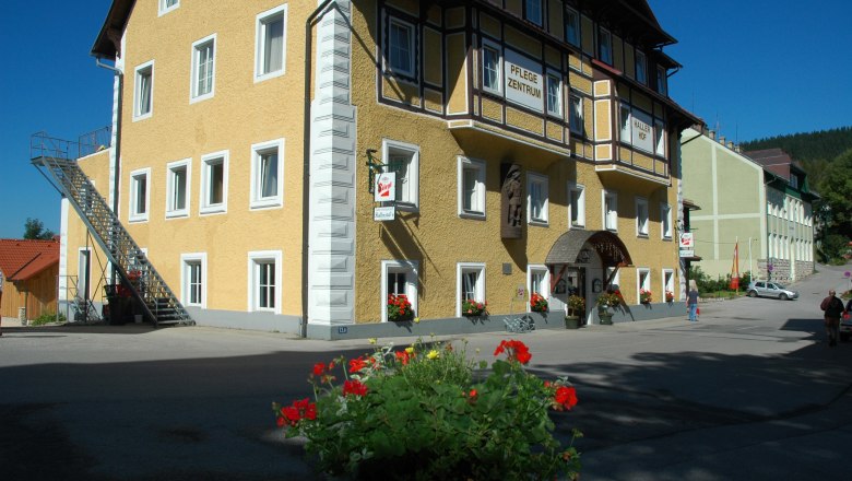 Yellow building with the inscription 'Hallerhof', flowers in the foreground.