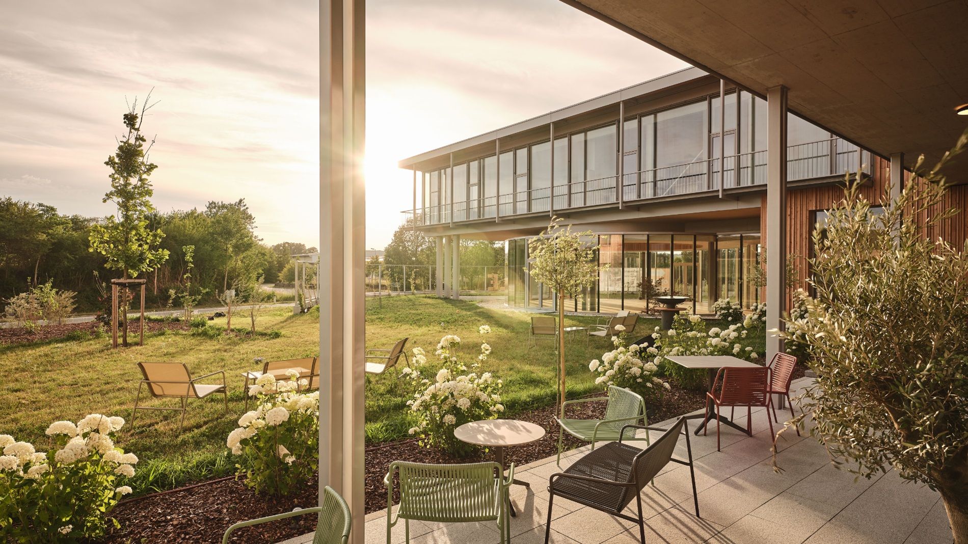 A modern patio with patio furniture and flowers in front of a building at sunset.