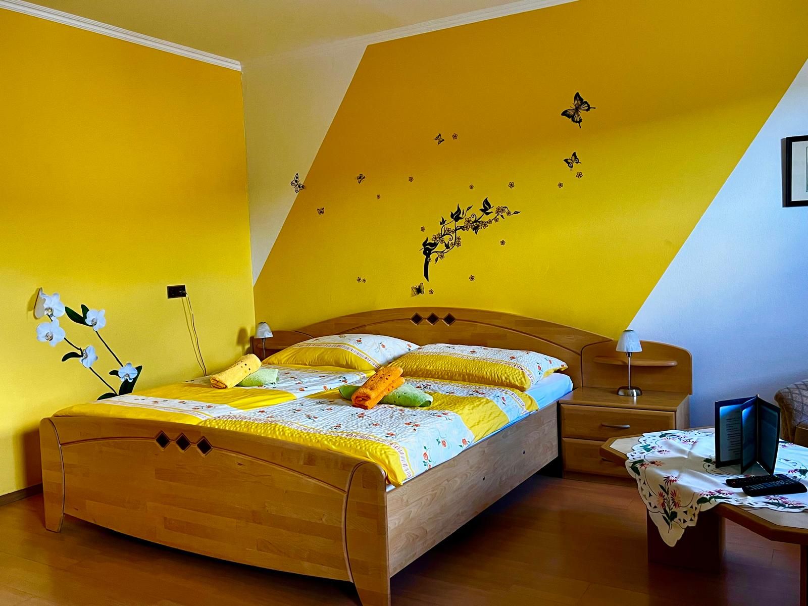 Cozy bedroom with yellow wall, double bed and decorative butterflies on the wall.