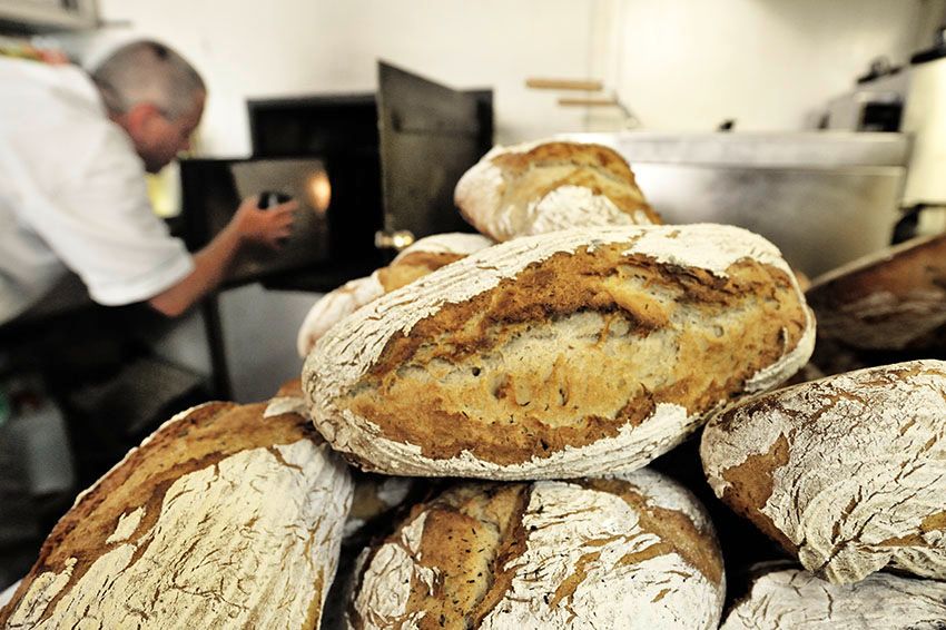 Freshly baked bread in front of a baker operating an oven.