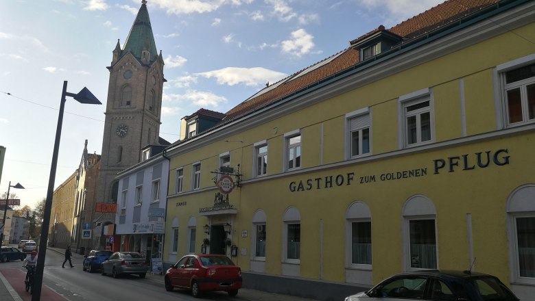 Street scene with yellow building 'Gasthof zum goldenen Pflug' and church tower in the background.
